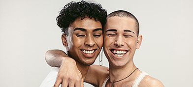 One person hugs their right arm around another person as both smile with their eyes closed.