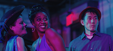 A still from "Lust Life Love" shows two laughing women and one serious man, all in pink and blue lighting. 