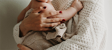 A woman in a knitted sweater holds a baby in her arms.
