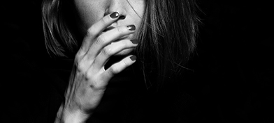 A woman with painted nails reaches her hand upward to cover her mouth.