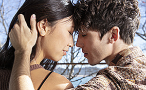 A couple sits on a bench outside while embraced.