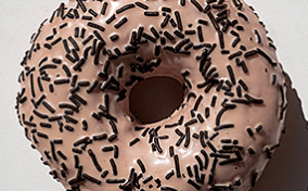 A pink donut with black sprinkles against a white background.