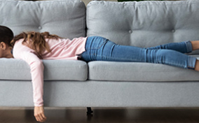 A woman lying on a grey couch tired from her period.