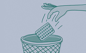 A hand throws away a packet of pills into a waste bin.