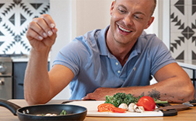 A man is putting a pinch of seasoning into a pan while cooking.