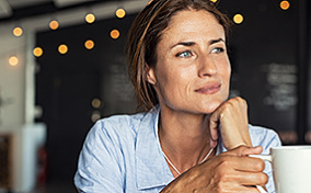 A woman holds a cup of tea and looks into the distance.