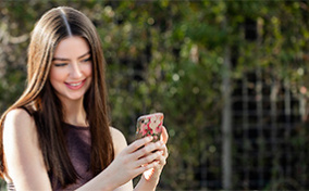 A woman looks at her phone smiling while taking a selfie.