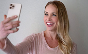 A woman smiles at her cellphone as she takes a selfie.