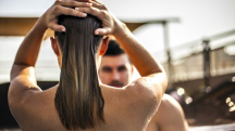 woman with wet hair runs her hands through it as she looks at a man on a beach